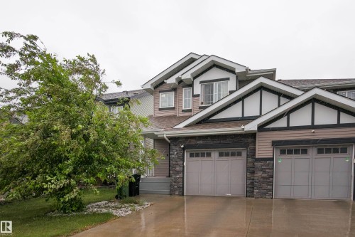 Modern townhome exterior featuring an attached two-car garage, stone façade accents, and neutral horizontal siding - 9468 209 St, Edmonton, AB 