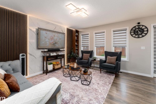 Living area featuring a distinctive accent wall with wood paneling and marble-finish detailing, integrated lighting, and wood-finish flooring - 9468 209 St, Edmonton, AB 