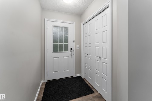 Entryway featuring a white paneled door with frosted glass inserts, bifold closet doors, light neutral wall paint, and wood-finish flooring - 9468 209 St, Edmonton, AB 