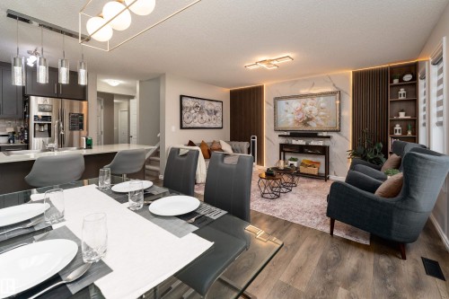 Open-concept living area featuring wood-finish flooring, a contemporary dining chandelier, and a kitchen island with pendant lighting - 9468 209 St, Edmonton, AB 