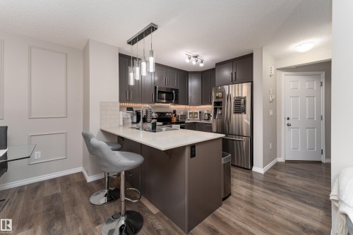 Contemporary kitchen featuring dark cabinetry, stainless steel appliances, and a central island with a breakfast bar - 9468 209 St, Edmonton, AB 