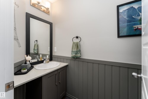 Bathroom featuring a single vanity with an integrated sink, dark wood-finish cabinetry, a light-toned countertop, and a framed mirror - 9468 209 St, Edmonton, AB 