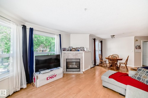 Living area featuring light wood-finish flooring, a corner fireplace with a tiled surround, and multiple windows providing natural light - 214 9938 104 Street, Edmonton, AB 