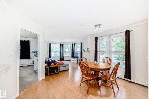 Open-concept living space featuring wood-finish flooring, white walls, and bright natural light from multiple windows - 214 9938 104 Street, Edmonton, AB 