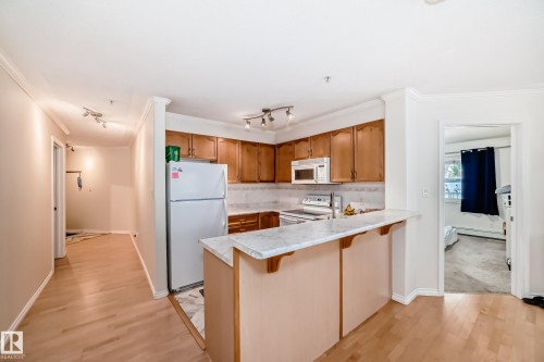 Kitchen featuring wood-finish cabinetry, white appliances, and a light-toned countertop with an integrated breakfast bar - 214 9938 104 Street, Edmonton, AB 