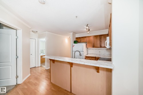 Kitchen featuring wood-finish cabinetry, a white refrigerator, and a stainless steel gooseneck faucet - 214 9938 104 Street, Edmonton, AB 