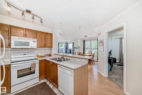 Kitchen featuring wood cabinetry, white appliances, track lighting, and a double basin sink - 214 9938 104 Street, Edmonton, AB 