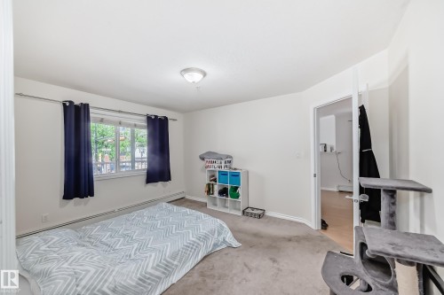 Carpeted room featuring a window with white trim, baseboard heating, a ceiling-mounted light fixture, and a solid-core door - 214 9938 104 Street, Edmonton, AB 