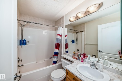 Full bathroom featuring a single vanity with a white oval sink, marble-finish countertop, and wood-finish cabinetry - 214 9938 104 Street, Edmonton, AB 