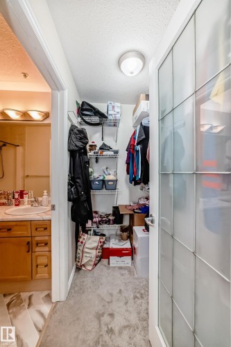 Walk-in closet featuring wire shelving, overhead lighting, and frosted glass paneled door - 214 9938 104 Street, Edmonton, AB 