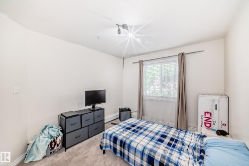 Carpeted room featuring a single window with blinds, a track light fixture, and white wall finishes - 214 9938 104 Street, Edmonton, AB 