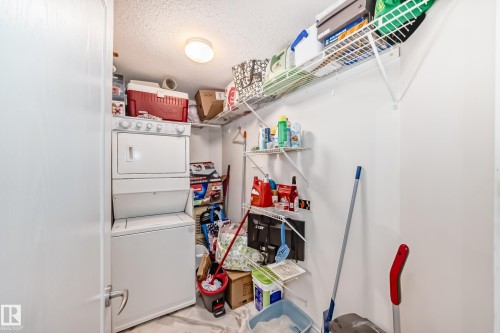 Dedicated utility space featuring a stacked washer and dryer, overhead flush-mount lighting, and wire shelving for storage - 214 9938 104 Street, Edmonton, AB 