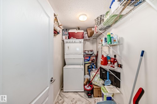 Dedicated laundry area with a stacked washer and dryer, ceiling-mounted light fixture, and built-in shelving - 214 9938 104 Street, Edmonton, AB 