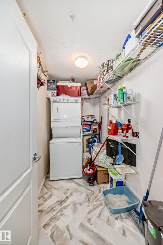 Laundry area featuring a stacked washer and dryer unit, wire shelving, and wood-finish flooring with a herringbone pattern - 214 9938 104 Street, Edmonton, AB 