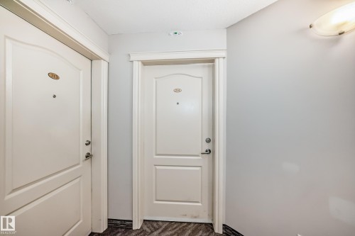Entryway featuring two panel doors with classic trim, light gray painted walls, and textured dark flooring - 214 9938 104 Street, Edmonton, AB 