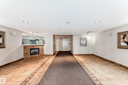 Entryway featuring a tiled floor with a decorative border, an integrated fireplace with a stone surround, recessed lighting, and a mirrored accent wall - 214 9938 104 Street, Edmonton, AB 