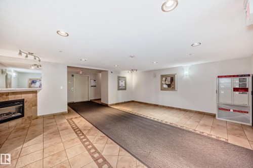 Lobby area featuring ceramic tile flooring with decorative inlay, a built-in electric fireplace with stone surround, recessed ceiling lighting, and wall-mounted light fixtures - 214 9938 104 Street, Edmonton, AB 