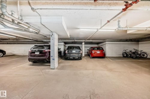 Underground parking space featuring concrete flooring, overhead fluorescent lighting, and exposed ceiling pipes - 214 9938 104 Street, Edmonton, AB 