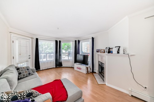 Bright living area featuring wood-finish flooring, a decorative fireplace with a mantel, a bay window, a glass-paned door, and crown molding - 214 9938 104 Street, Edmonton, AB 