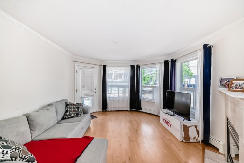 Living area featuring wood-finish flooring, a bay window with multiple panes, a white trim package, and a built-in fireplace - 214 9938 104 Street, Edmonton, AB 