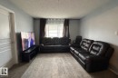 Living area featuring light gray walls, textured ceiling, a white paneled door, and a window with blinds and drapes - 133 301 Clareview Station Drive, Edmonton, AB 