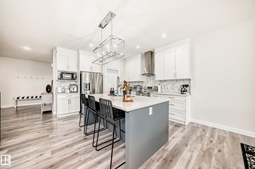 Modern kitchen featuring a central island with a light-toned countertop and contrasting base, white shaker-style cabinetry, and wood-finish flooring - 589 Boulder Wynd, Leduc, AB - Indoor Photo Showing Kitchen With Upgraded Kitchen