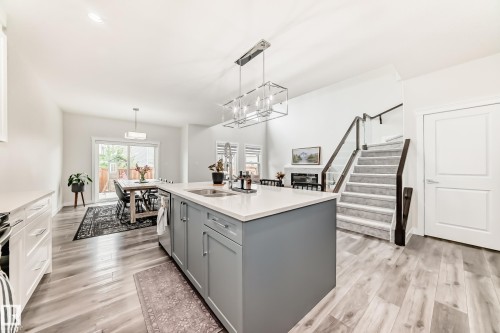 Spacious open-concept living area featuring a central island kitchen, wood-finish flooring, and a glass-paneled staircase - 589 Boulder Wynd, Leduc, AB - Indoor Photo Showing Kitchen With Double Sink