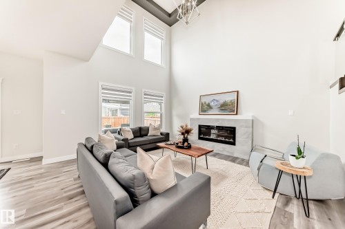 Vaulted living space featuring high ceilings, wood-finish flooring, and an electric fireplace with a stone surround - 589 Boulder Wynd, Leduc, AB - Indoor Photo Showing Living Room With Fireplace