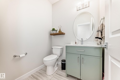 Powder room featuring a sage green vanity with a white countertop and integrated sink, an oval mirror, and a contemporary wall-mounted light fixture - 589 Boulder Wynd, Leduc, AB - Indoor Photo Showing Bathroom