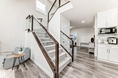 Modern staircase featuring a glass and wood-finish railing, carpeted treads, and a prominent window - 589 Boulder Wynd, Leduc, AB - Indoor Photo Showing Other Room