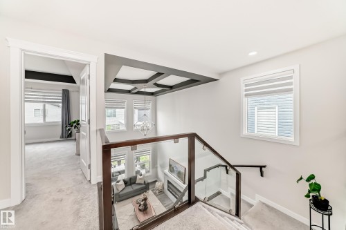 Upper-level landing featuring a glass railing, coffered ceiling detail, and carpeted flooring - 589 Boulder Wynd, Leduc, AB - Indoor Photo Showing Other Room