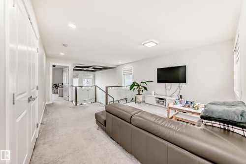 Upper-level living area featuring light gray carpeting, recessed ceiling lighting, a contemporary glass and metal railing system, white interior doors with polished chrome hardware, and large windows with horizontal blinds - 589 Boulder Wynd, Leduc, AB - Indoor