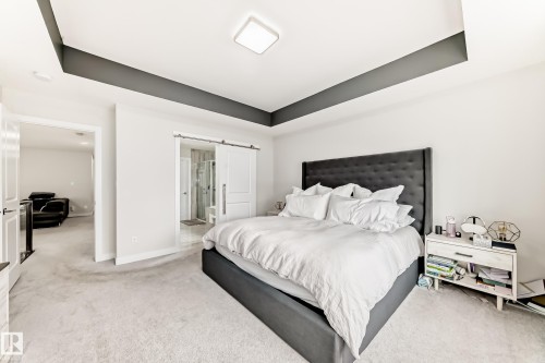 Recessed ceiling with contrasting dark accent, light-toned carpeting, and a modern square flush-mount light fixture - 589 Boulder Wynd, Leduc, AB - Indoor Photo Showing Bedroom