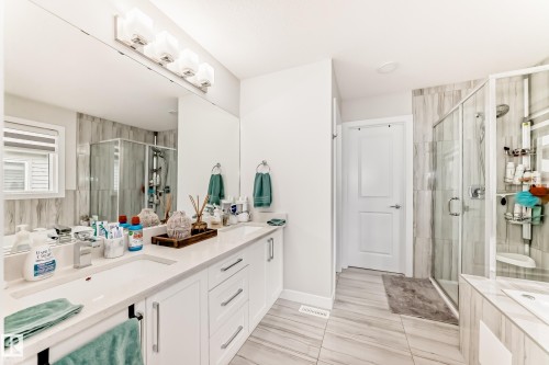 Bathroom featuring a double vanity with stone countertops, white shaker cabinetry, and dual undermount sinks - 589 Boulder Wynd, Leduc, AB - Indoor Photo Showing Bathroom