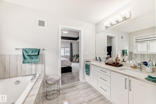 Bathroom featuring a dual vanity with white cabinetry, light-toned countertops, and a full-width mirror - 589 Boulder Wynd, Leduc, AB - Indoor Photo Showing Bathroom
