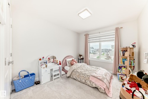 Bright room featuring light gray carpet flooring, white walls, a large window with horizontal blinds and pink drapes, and a contemporary ceiling light fixture - 589 Boulder Wynd, Leduc, AB - Indoor Photo Showing Bedroom