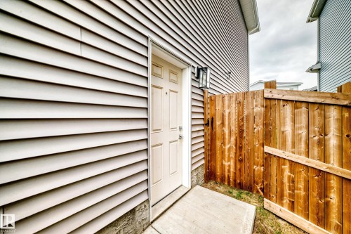 Private side entrance featuring a privacy fence, concrete walkway, and exterior wall lantern - 589 Boulder Wynd, Leduc, AB - Outdoor