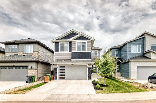 Contemporary exterior with multi-toned siding, stone accents, a landscaped front yard, a single-car garage with a modern door, and a concrete driveway - 589 Boulder Wynd, Leduc, AB - Outdoor With Facade