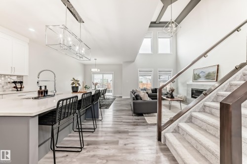 Open-concept interior featuring light wood-finish flooring, a two-story ceiling, and a prominent staircase with glass railing - 589 Boulder Wynd, Leduc, AB - Indoor Photo Showing Kitchen With Upgraded Kitchen