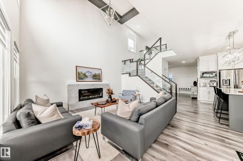 Living area with soaring ceilings, a modern linear fireplace with a light-toned surround, and expansive windows - 589 Boulder Wynd, Leduc, AB - Indoor Photo Showing Living Room With Fireplace