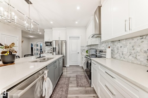 Bright kitchen featuring an expansive center island with an undermount dual sink, white countertops, stainless steel appliances, and a mosaic tile backsplash - 589 Boulder Wynd, Leduc, AB - Indoor Photo Showing Kitchen With Double Sink