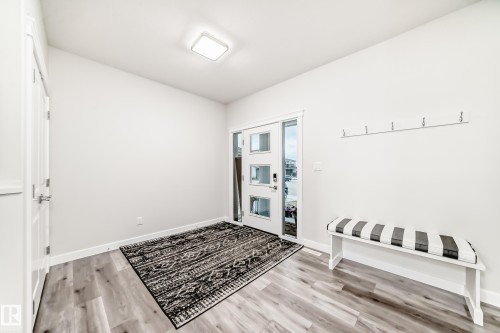 Entryway featuring wood-finish flooring, a modern square ceiling light fixture, and a white paneled door with rectangular glass inserts - 589 Boulder Wynd, Leduc, AB - Indoor Photo Showing Other Room