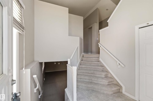 Split-level entry featuring light gray walls, white trim, a carpeted staircase with white railings, and a white paneled door - 2012 35A Avenue, Edmonton, AB 