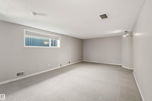 Spacious room featuring light gray carpeting, neutral wall paint, a single window with blinds, baseboard trim, and a three-bulb track lighting fixture - 2012 35A Avenue, Edmonton, AB 