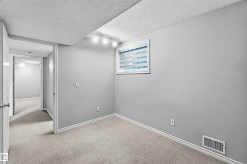 Carpeted room featuring a window with horizontal blinds, track lighting, and a baseboard vent - 2012 35A Avenue, Edmonton, AB 