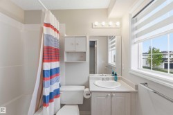 Bathroom featuring a single vanity with a white countertop and base cabinetry, a bathtub with a shower, a wall-mounted storage cabinet, and a window with blinds - 