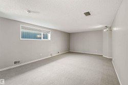 Spacious room featuring light gray carpeting, neutral wall paint, a single window with blinds, baseboard trim, and a three-bulb track lighting fixture - 