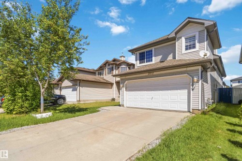 Two-story residence featuring light gray siding, an attached garage with a white panel door, a concrete driveway, and a partially fenced yard - 2012 35A Avenue, Edmonton, AB 