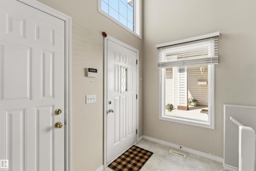 Foyer featuring a white paneled entry door with decorative glass inserts, a white paneled interior door, an upper transom window, and a large window with white blinds - 2012 35A Avenue, Edmonton, AB 