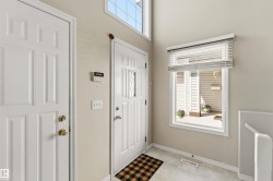 Foyer featuring a white paneled entry door with decorative glass inserts, a white paneled interior door, an upper transom window, and a large window with white blinds - 
